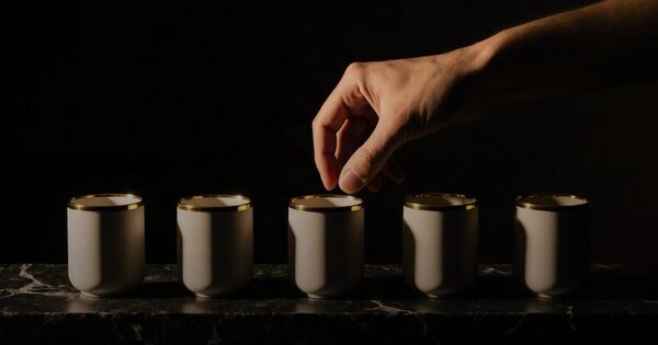 A hand placing the last of five plain ceramic vessels into one curated row on dark stone