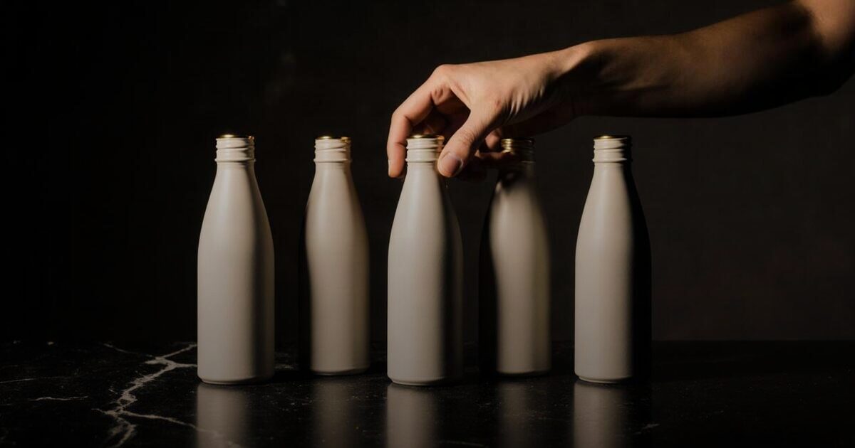 A hand turning one of five identical unlabelled bottles lined up on dark marble