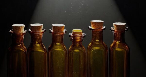 A row of identical unlabeled amber glass bottles with one lit by a narrow spotlight beam
