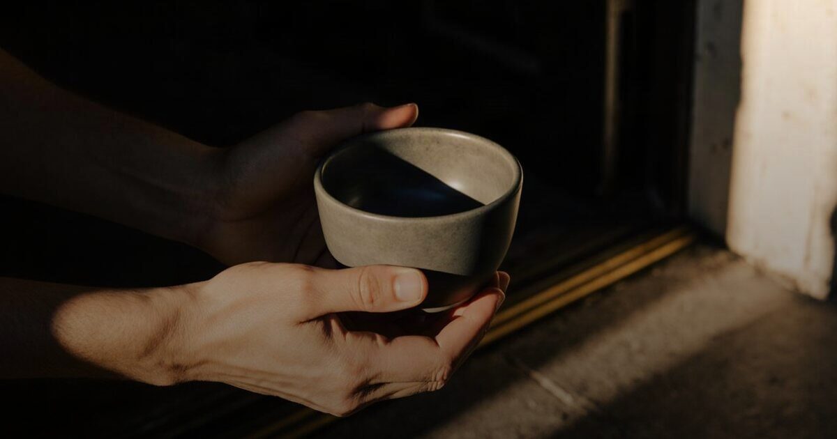 Hands passing a plain ceramic vessel to open palms at a sunlit doorway
