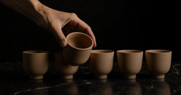 A hand lifting one plain ceramic vessel out of a row of five for close inspection