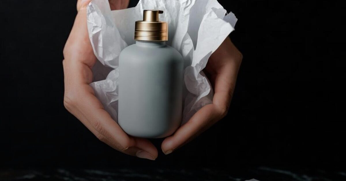 Two hands cradling a plain unlabeled bottle nested in soft white tissue paper